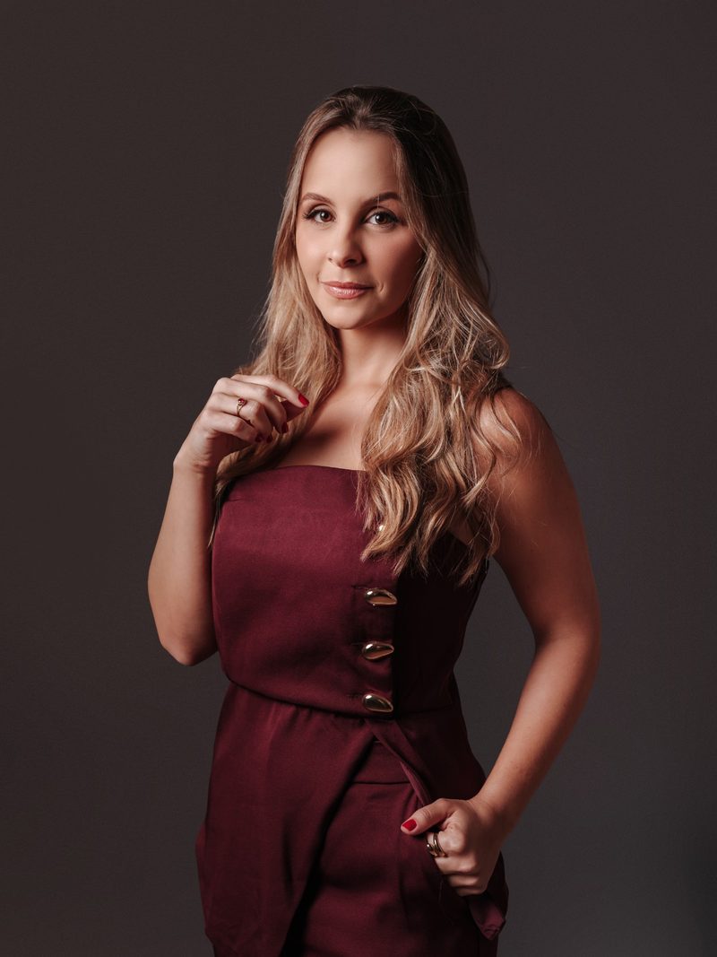 Mariana de Paula Araújo, advogada trabalhista, em retrato de meio corpo com vestido bordô de botões dourados.